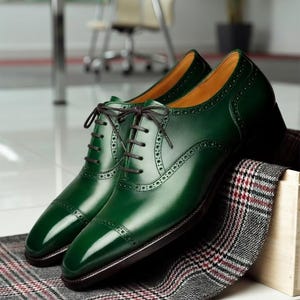 May include: A pair of polished, emerald green leather dress shoes with brown laces. The shoes feature a classic cap-toe design and decorative perforations. They rest on a patterned fabric, suggesting a focus on formal footwear.