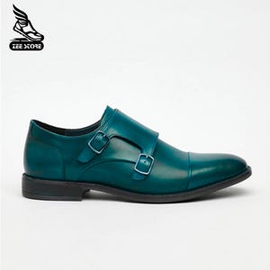 May include: Teal leather double monk strap dress shoe with a cap toe. The shoe features two adjustable buckles and a black sole. The Zee Store logo is in the upper left corner.