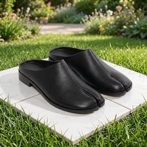 May include: A pair of black leather mules featuring a distinctive split-toe design. These slip-on shoes have a smooth finish, a low heel, and a seam running down the center of the vamp, creating a clean and structured appearance for the footwear.