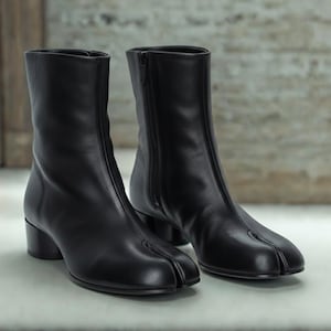 May include: A pair of black leather ankle boots with a split-toe design. The boots have a side zipper and a small block heel. The boots are approximately 6 inches tall.
