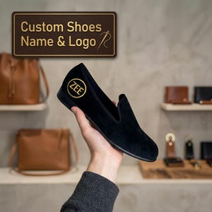May include: A black velvet slip-on shoe featuring a gold embroidered circular logo with the text ZEE on the side. Above the shoe, a rectangular sign with a brown background displays the gold text Custom Shoes Name & Logo.