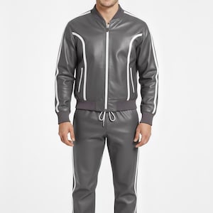 Peut inclure: Un surv&ecirc;tement en cuir gris avec des rayures et des bordures blanches. La veste a une fermeture &eacute;clair et des passepoils blancs le long des manches et des &eacute;paules. Le pantalon a une taille &agrave; cordon et des rayures blanches sur les c&ocirc;t&eacute;s. Port&eacute; par une personne.