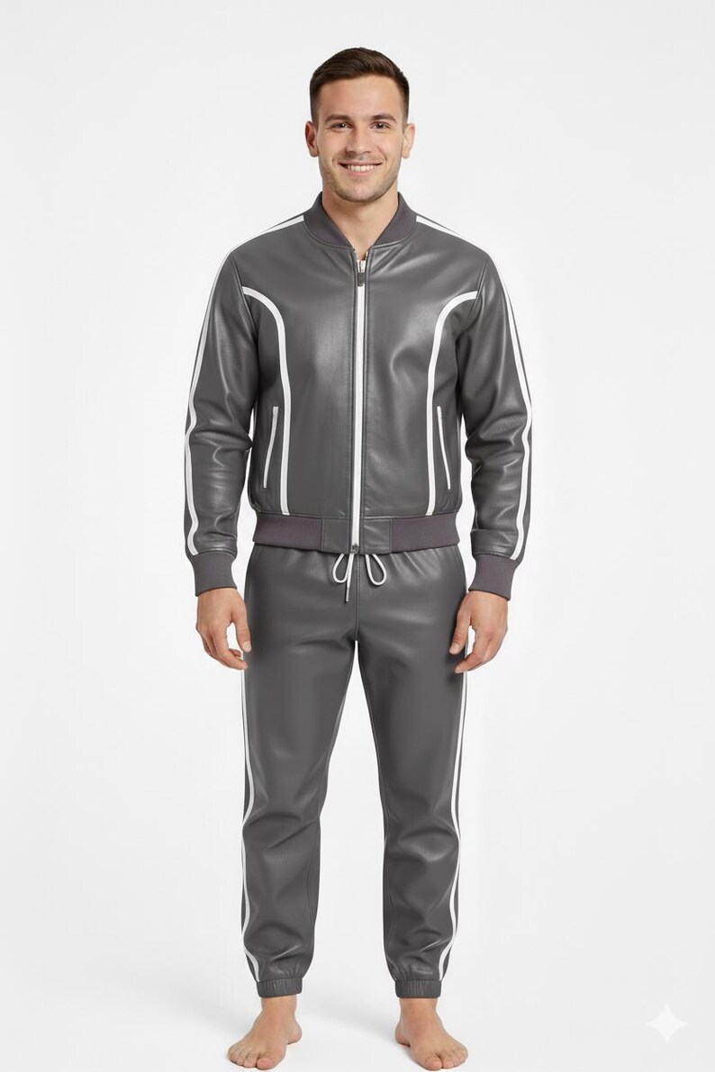 Peut inclure: Un surv&ecirc;tement en cuir gris avec des rayures et des bordures blanches. La veste a une fermeture &eacute;clair et des passepoils blancs le long des manches et des &eacute;paules. Le pantalon a une taille &agrave; cordon et des rayures blanches sur les c&ocirc;t&eacute;s. Port&eacute; par une personne.