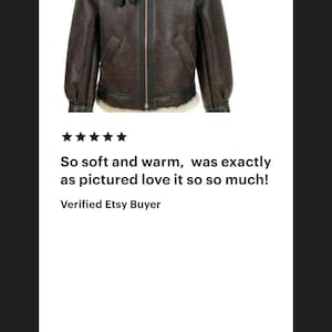 K&ouml;nnte beinhalten: Eine dunkelbraune Lederjacke mit einem cremefarbenen Lammfellkragen und Innenfutter. Die Jacke verf&uuml;gt &uuml;ber einen zentralen Rei&szlig;verschluss, zwei Seitentaschen sowie schwarze Lederbesatzdetails entlang der N&auml;hte und an den &Auml;rmelb&uuml;ndchen.