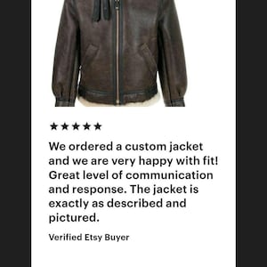 K&ouml;nnte beinhalten: Eine dunkelbraune Lederjacke mit einem cremefarbenen Lammfellkragen, einem zentralen Rei&szlig;verschluss und zwei schwarzen Lederriemen mit Schnallen am Hals. Die Jacke hat lange &Auml;rmel und einen am unteren Rand sichtbaren Lammfellsaum.