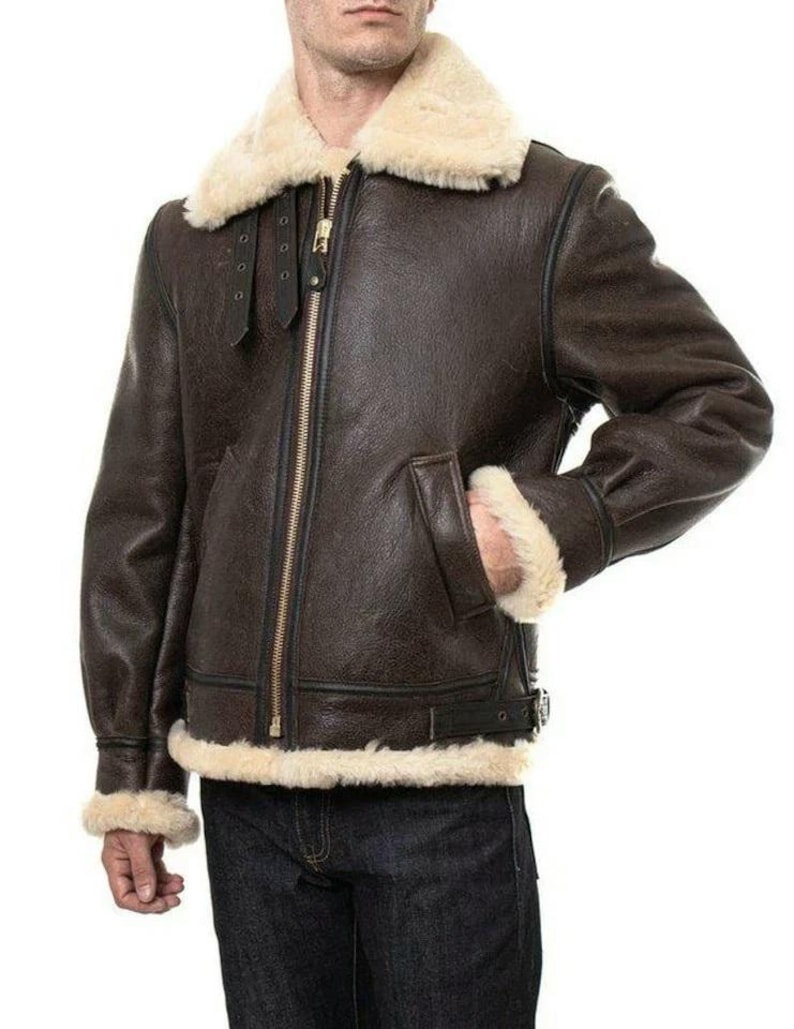 K&ouml;nnte beinhalten: Eine dunkelbraune Leder-Bomberjacke mit einem dicken, cremefarbenen Lammfellkragen sowie passenden &Auml;rmelb&uuml;ndchen und Saum. Die Jacke verf&uuml;gt &uuml;ber einen goldenen Frontrei&szlig;verschluss, zwei Seitentaschen und schwarze Lederriemendetails.