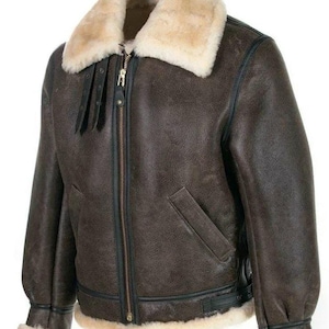 K&ouml;nnte beinhalten: Eine dunkelbraune Lederjacke mit einem dicken, cremefarbenen Lammfellkragen und &Auml;rmelb&uuml;ndchen. Die Jacke verf&uuml;gt &uuml;ber einen zentralen Metallrei&szlig;verschluss, zwei schr&auml;ge Vordertaschen, schwarze Lederbes&auml;tze und zwei kleine verstellbare Riemen am Kragen.