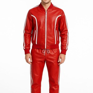 Peut inclure: Ensemble de surv&ecirc;tement en cuir rouge avec des rayures blanches. La veste a une fermeture &eacute;clair et un col de style bombardier. Le pantalon a une taille &agrave; cordon et une coupe droite. Port&eacute; par une personne.