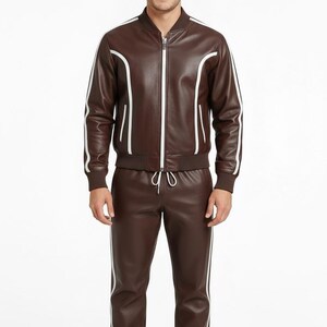 Peut inclure: Un surv&ecirc;tement en cuir marron avec des rayures blanches. La veste a une fermeture &eacute;clair et des bordures blanches. Le pantalon a une taille &agrave; cordon et des rayures blanches sur les c&ocirc;t&eacute;s. L'ensemble est port&eacute; par une personne.