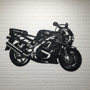 Pode incluir: Silhueta preta de motocicleta montada em uma parede de tijolos brancos. A motocicleta apresenta elementos de design detalhados, incluindo as rodas, o escapamento e a carenagem. O logotipo da Honda é visível. Uma peça decorativa para entusiastas de motocicletas.