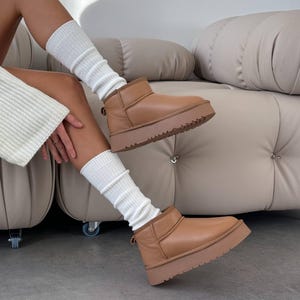 Puede incluir: Botas de plataforma color canela con punta redondeada y suela gruesa. Las botas tienen caña corta y una lengüeta en la parte trasera. Las botas se llevan con calcetines blancos de canalé.