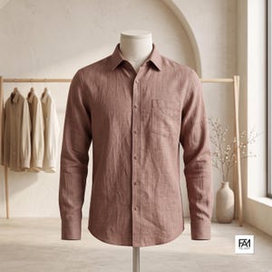 May include: A long-sleeved button-down shirt in a muted dusty rose color, featuring a classic collar, a single chest pocket on the left side, and a buttoned front placket. The shirt is displayed on a mannequin, showcasing a textured fabric finish.