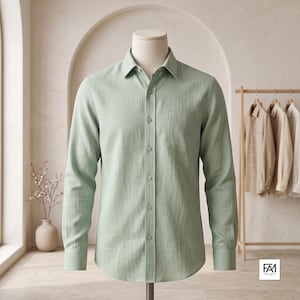 May include: A light sage green long-sleeve button-down shirt displayed on a mannequin. The shirt features a classic collar, a single chest pocket on the left side, and matching green buttons running down the center placket and on the cuffs.