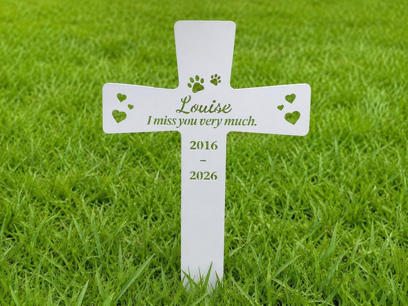 May include: A white cross-shaped memorial marker featuring the name Louise, the text I miss you very much, the years 2016-2026, two paw prints, and four heart-shaped cutouts. The marker is designed to be inserted into the ground.