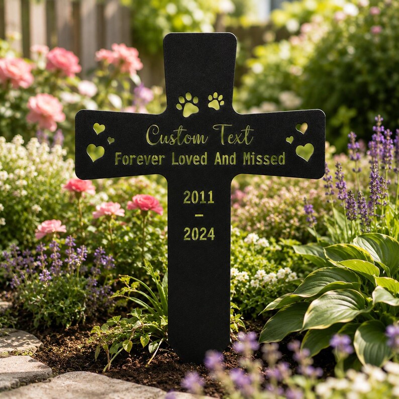 May include: A black metal cross garden stake featuring laser-cut details including two paw prints at the top, four heart-shaped cutouts, and engraved text reading Custom Text, Forever Loved And Missed, 2011, and 2024 in a gold-toned finish.