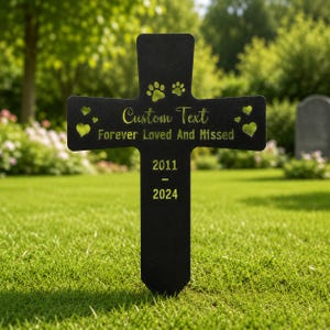 May include: A black metal cross-shaped memorial stake featuring cut-out paw prints and heart shapes. The text reads Custom Text, Forever Loved And Missed, 2011, and 2024 in a light yellow font. The design includes a pointed base for ground insertion.