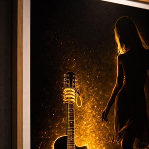May include: Acoustic guitar art print. The black guitar is illuminated with golden light, with a woman's silhouette in the background. The guitar's headstock is wrapped in a string of lights. The artwork is framed in a light wood frame.