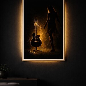 May include: Acoustic guitar art print with a silhouette of a person. The guitar is illuminated with a warm glow, set against a dark background. The artwork is framed with a light border, creating a striking visual.