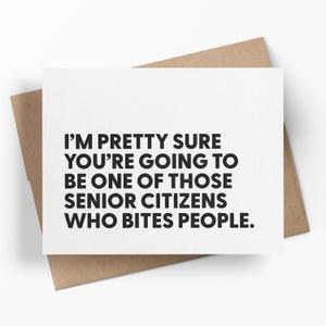 May include: A white greeting card with the text "I'M PRETTY SURE YOU'RE GOING TO BE ONE OF THOSE SENIOR CITIZENS WHO BITES PEOPLE." is placed on a brown envelope. The text is in a bold, black font.