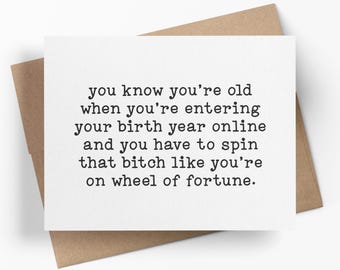 May include: A white rectangular greeting card with black typewriter-style text that reads: you know you're old when you're entering your birth year online and you have to spin that bitch like you're on wheel of fortune. The card sits on a brown envelope.