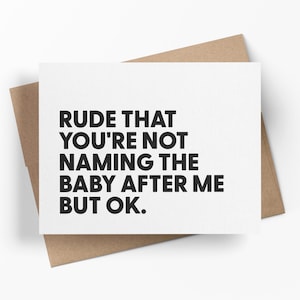 May include: A white greeting card with the text "RUDE THAT YOU'RE NOT NAMING THE BABY AFTER ME BUT OK." in black, set against a brown envelope. The card is angled, showing the envelope's texture.