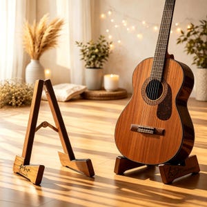 Puede incluir: Guitarra acústica sobre un soporte de madera. La guitarra es marrón con un golpeador marrón oscuro y una boca. El soporte es de madera y tiene una inscripción personalizada. También se ve otro soporte de madera.