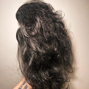 May include: A dark gray wig with wavy, layered hair. The wig has a natural look with some lighter gray strands mixed in. The hair is styled with volume and texture, creating a full and realistic appearance.