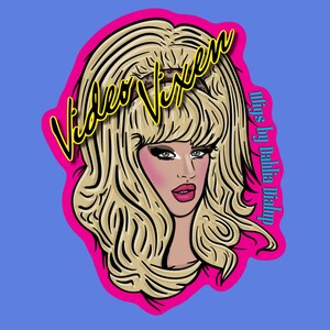 May include: A digital illustration of a woman with blonde hair, pink blush, and red lipstick. The image is framed by a pink border and features the text "Video Vixen" in yellow and "wigs by Dahlia Dialup" in purple.