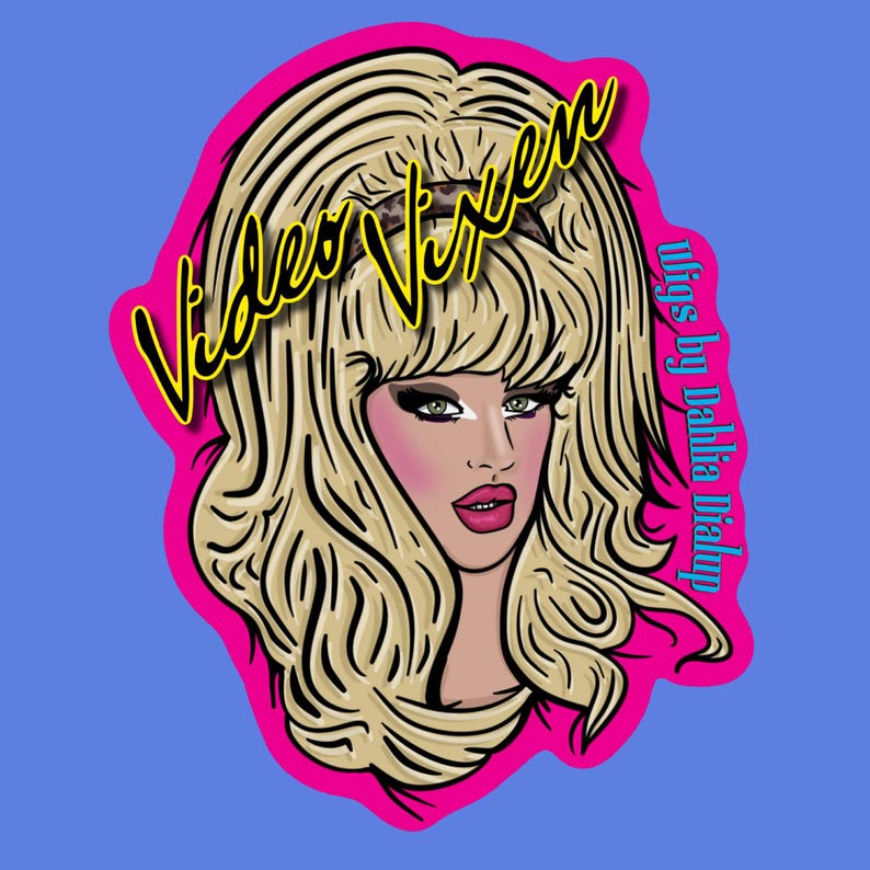 May include: A digital illustration of a woman with blonde hair, pink blush, and red lipstick. The image is framed by a pink border and features the text "Video Vixen" in yellow and "wigs by Dahlia Dialup" in purple.
