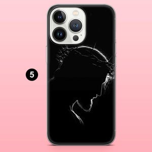 May include: Black phone case featuring a white silhouette of a person wearing a crown of thorns. The design is a profile view against a black background. The phone case has a clear border and a pink background.