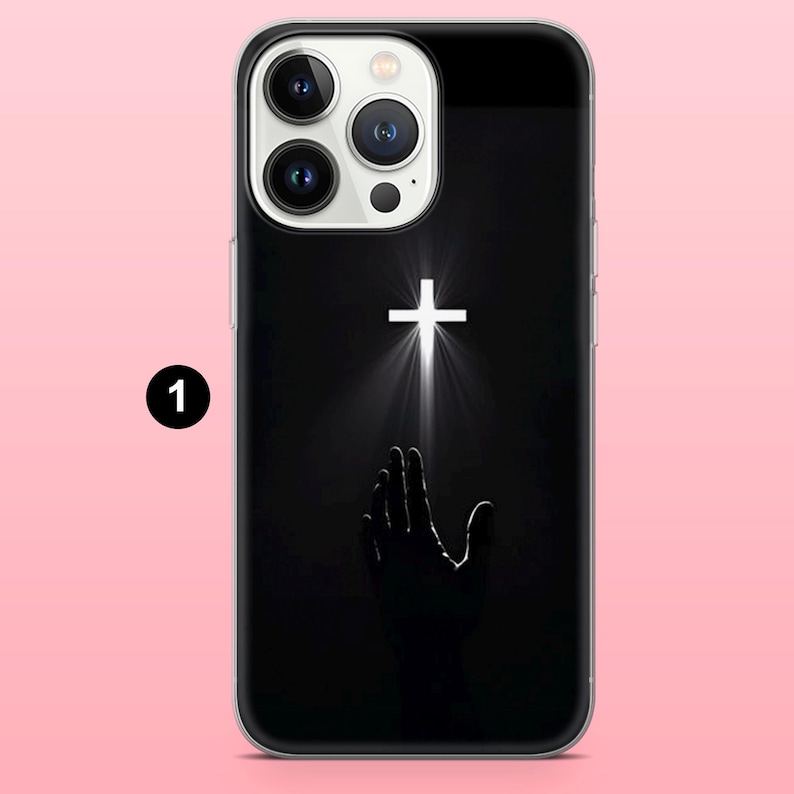 May include: Black phone case featuring a white cross with light rays emanating from it, above a silhouetted hand reaching upwards. The case has a clear border and a black background.