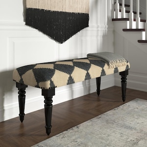 May include: Upholstered bench with a geometric pattern in black and beige. The bench has black, turned legs and is accented with nailhead trim. A gray throw blanket rests on the bench. A decorative wall hanging is above the bench.