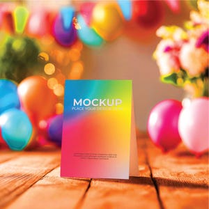 May include: A colorful mockup card with the word "MOCKUP" in white, set against a vibrant gradient background of blue, green, yellow, orange, and pink. The card is on a wooden surface, with balloons and flowers in the background.