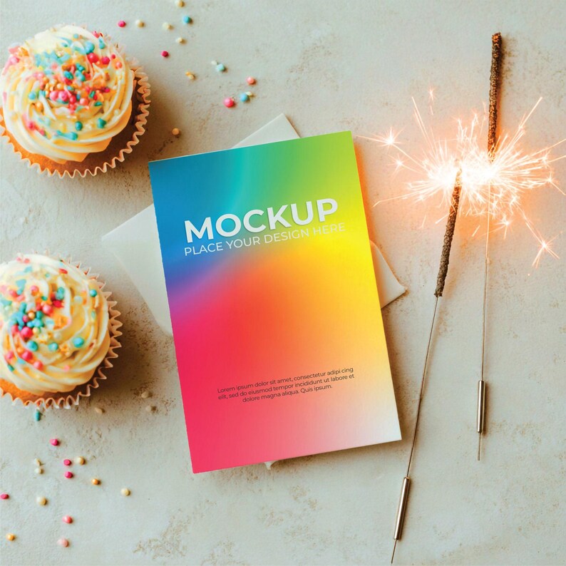 May include: A mockup card with a vibrant rainbow gradient, the text "MOCKUP PLACE YOUR DESIGN HERE" is displayed. Two cupcakes with colorful sprinkles and a lit sparkler are also present on a light gray surface.