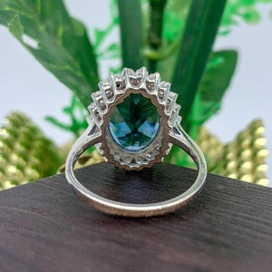 Oval blue sapphire cocktail ring with sparkling halo stones and polished silver band.