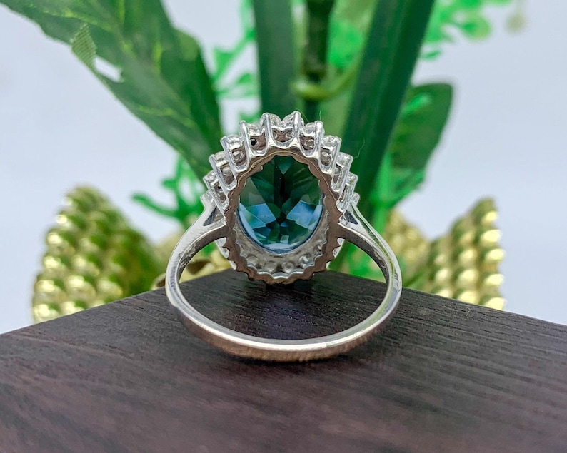Oval blue sapphire cocktail ring with sparkling halo stones and polished silver band.