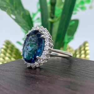 Side profile of a lab-created blue sapphire halo ring in sterling silver showing the elevated basket setting and oval blue gemstone