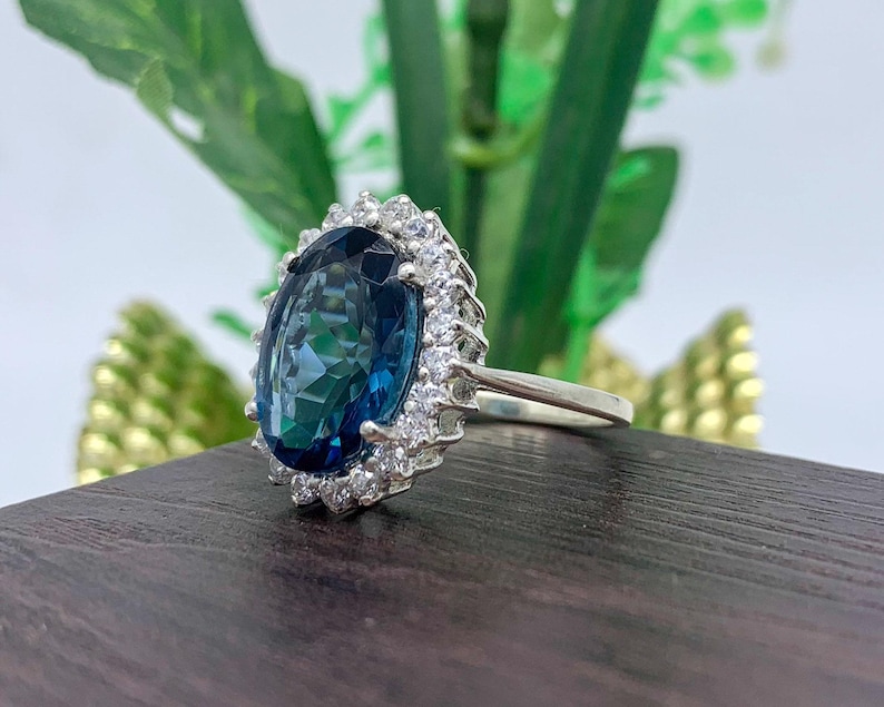 Side profile of a lab-created blue sapphire halo ring in sterling silver showing the elevated basket setting and oval blue gemstone