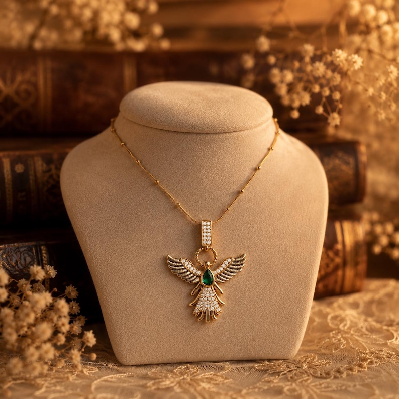 Close-up view of angel wing pendant with green stone on delicate gold chain.