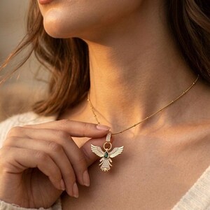 Gold angel wing pendant necklace with green teardrop stone and sparkling cubic zirconia details.