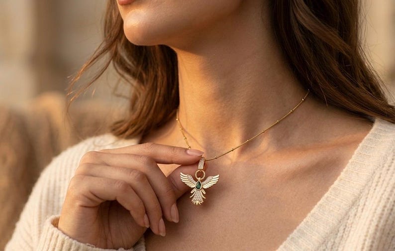 Gold angel wing pendant necklace with green teardrop stone and sparkling cubic zirconia details.
