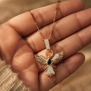 Dainty gold angel pendant necklace displayed in luxury handheld jewelry photography.