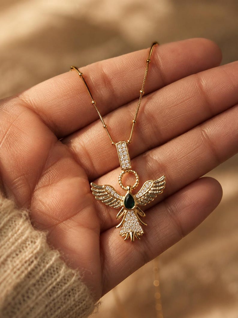 Dainty gold angel pendant necklace displayed in luxury handheld jewelry photography.