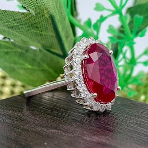Side profile of a lab-created ruby halo ring in sterling silver showing the elevated basket setting and oval red gemstone