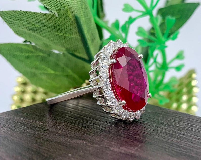 Side profile of a lab-created ruby halo ring in sterling silver showing the elevated basket setting and oval red gemstone