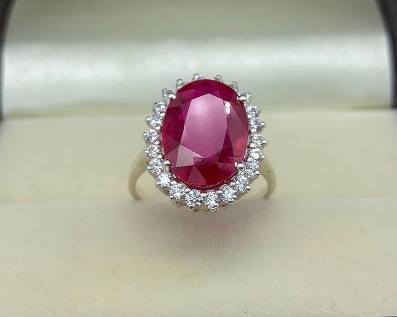 Close-up of an oval lab-created ruby ring with a sparkling halo setting in polished sterling silver.