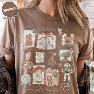 May include: Espresso-colored t-shirt featuring a collage of Toy Story characters and imagery. The design includes Woody, Buzz Lightyear, and other characters in a postage stamp style. Text includes "Toy Story" and "You've Got a Friend in Me."