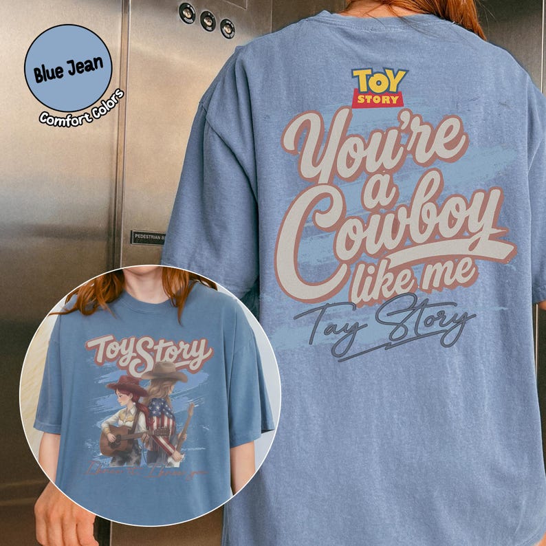 May include: A blue jean colored t-shirt featuring the Toy Story logo and the text "You're a Cowboy like me" on the back. The front graphic displays two figures with guitars and the text "Toy Story" in a stylized font with a blue brushstroke background.