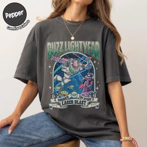 Puede incluir: Camiseta gris oscuro con un gr&aacute;fico de Buzz Lightyear de Toy Story. El dise&ntilde;o incluye a Buzz con su traje espacial, extraterrestres y el texto "Buzz Lightyear" y "Laser Blast". La camiseta tiene un aspecto vintage.