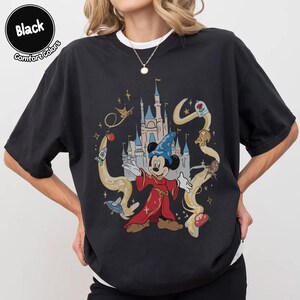 May include: Black t-shirt with a graphic of Mickey Mouse as a sorcerer, set against a castle and magical imagery. The shirt includes the words "Black" and "Comfort Colors" in a circular design.